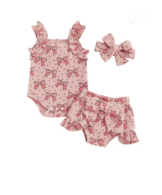 Baby outfit set with pink romper and bloomers featuring bow patterns, accompanied by a matching headband on a white background.