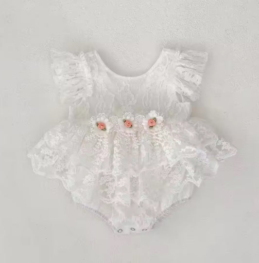 White lace baby romper with floral details on a light gray background