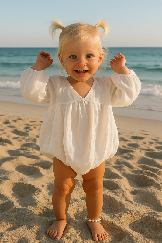 Child in a white outfit standing on a sandy beach with ocean in the background