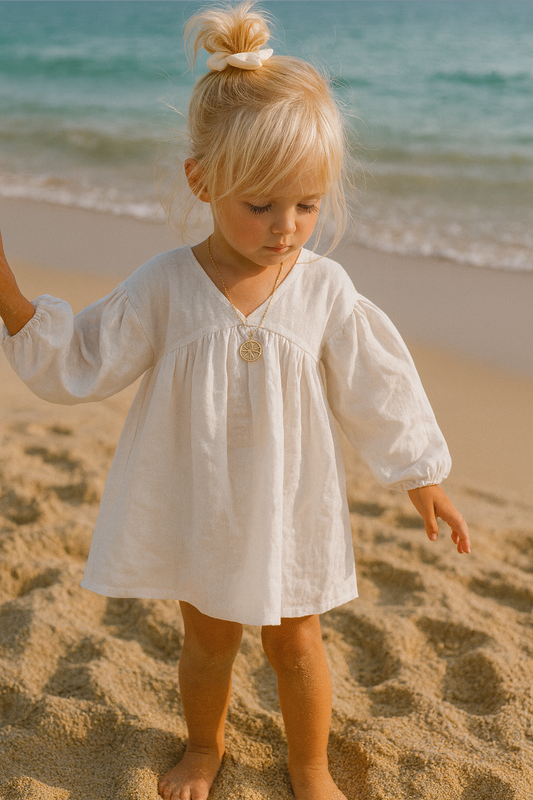 Child in a white dress standing on a sandy beach with ocean waves in the background