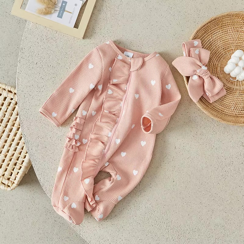 Pink baby outfit with heart patterns on a beige surface