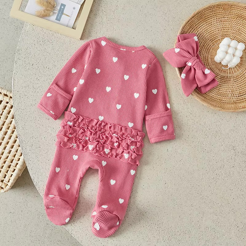 Pink baby outfit with heart patterns on a beige surface