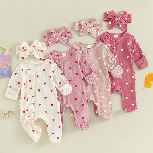 Set of baby rompers with heart patterns and matching headbands on a light background
