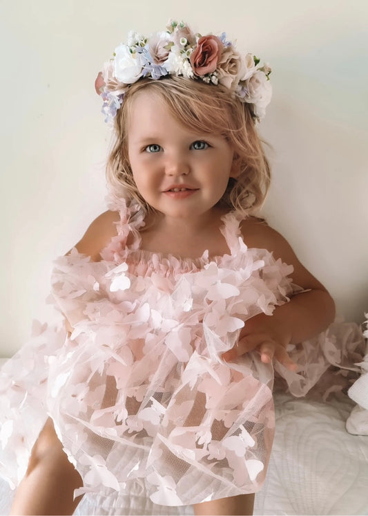 Young child wearing a floral headband and pink ruffled dress against a white background