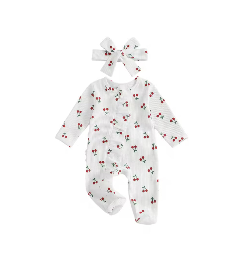A baby footed romper in white ribbed fabric with a small red cherry print, shown with a matching white bow headband on a plain white background.