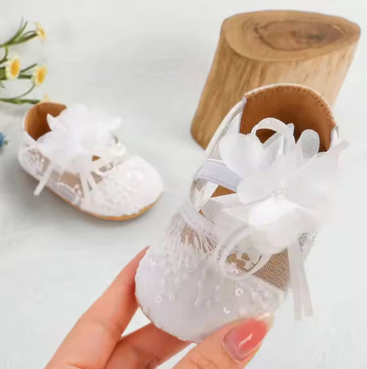 White baby shoes with lace details held by a hand against a light background