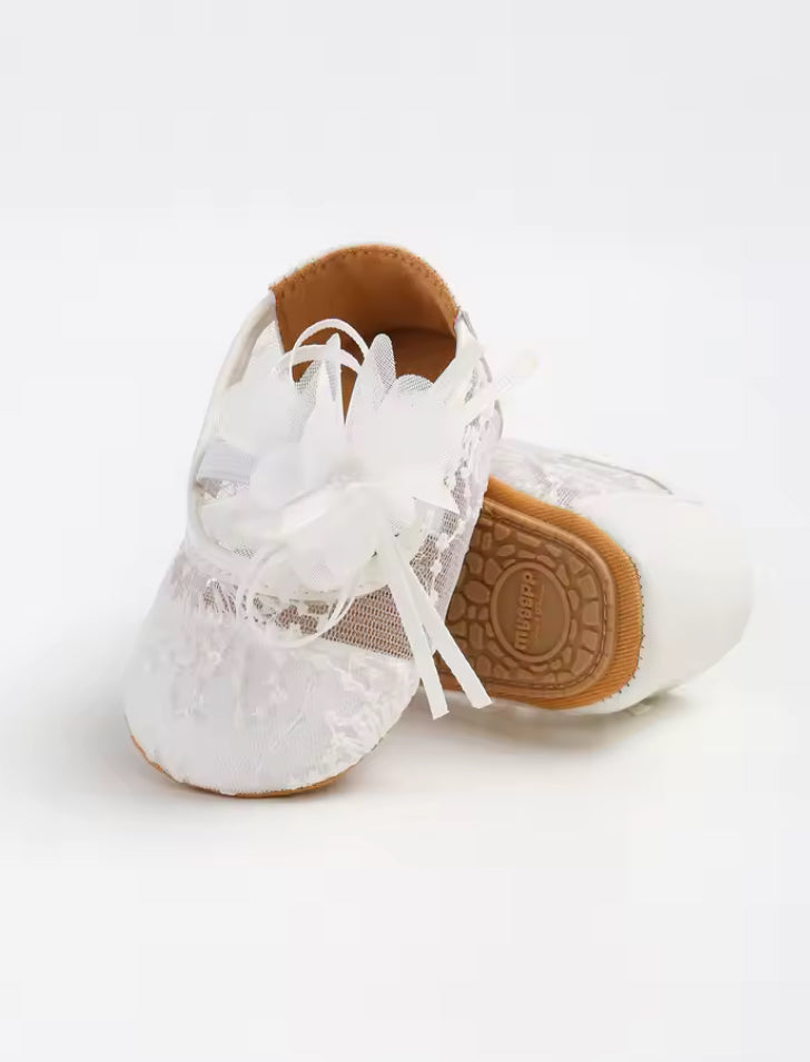 White baby shoes with lace details on a white background