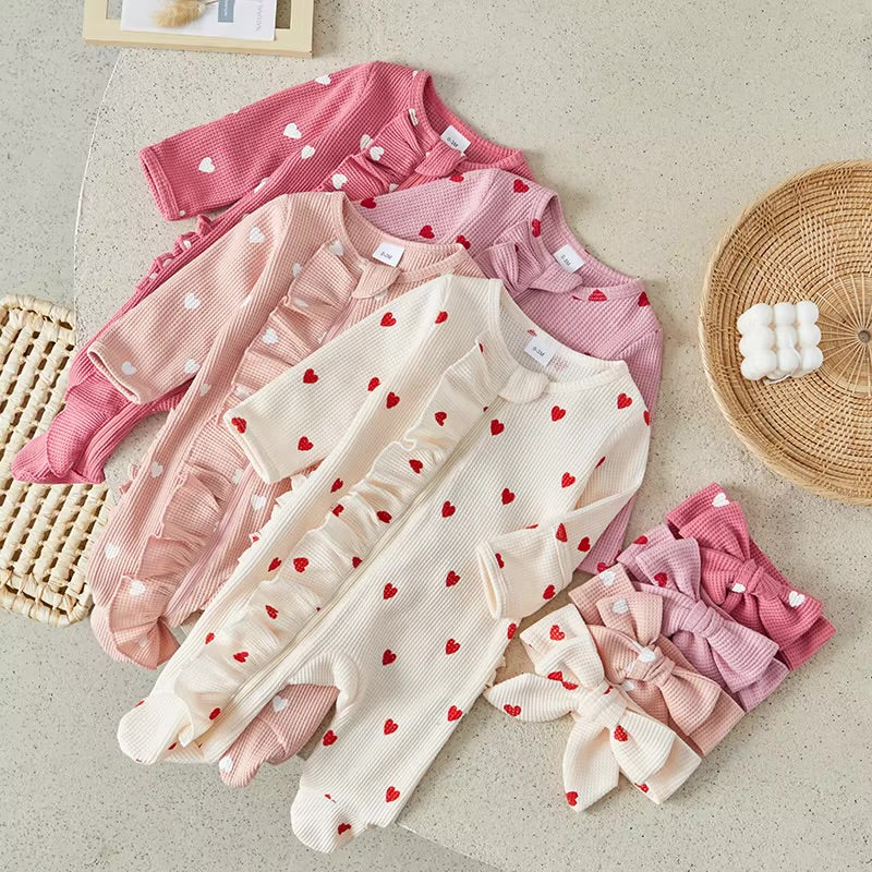 Set of baby rompers with heart patterns on a light surface