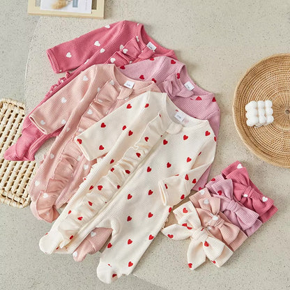 Set of baby rompers with heart patterns on a light surface