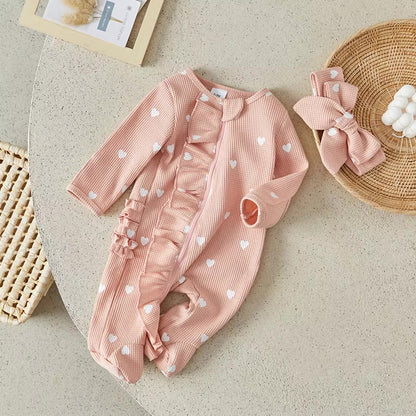 Pink baby outfit with heart patterns on a beige surface