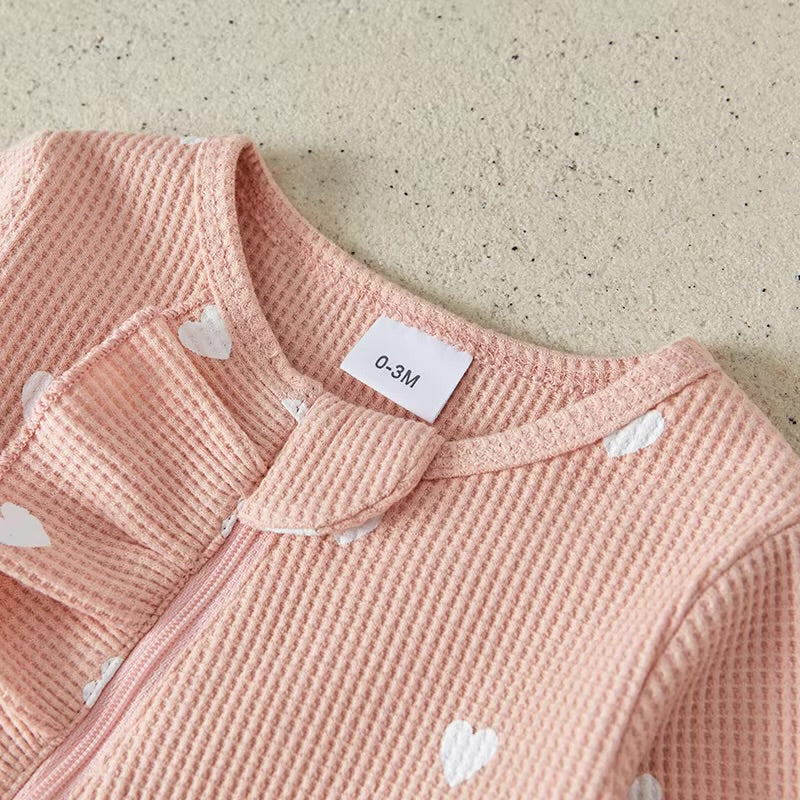 Pink textured garment with heart patterns and a size label on a beige background