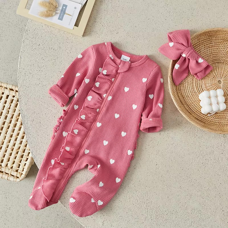 Pink baby romper with white heart patterns on a beige surface