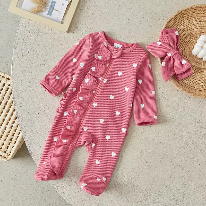 Pink baby romper with heart patterns and matching headband on a neutral surface