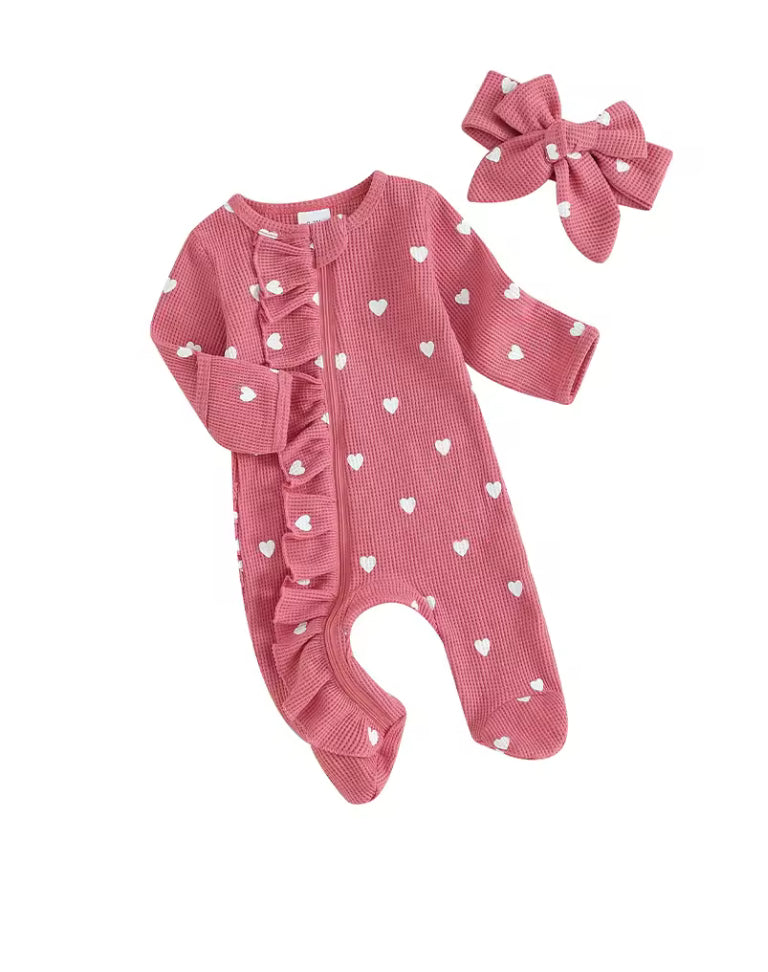 Pink baby romper with white heart patterns and matching headband on a white background