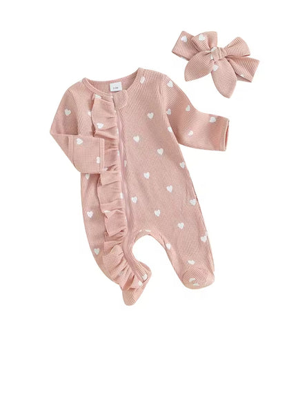 Pink baby romper with heart patterns and matching headband on a white background