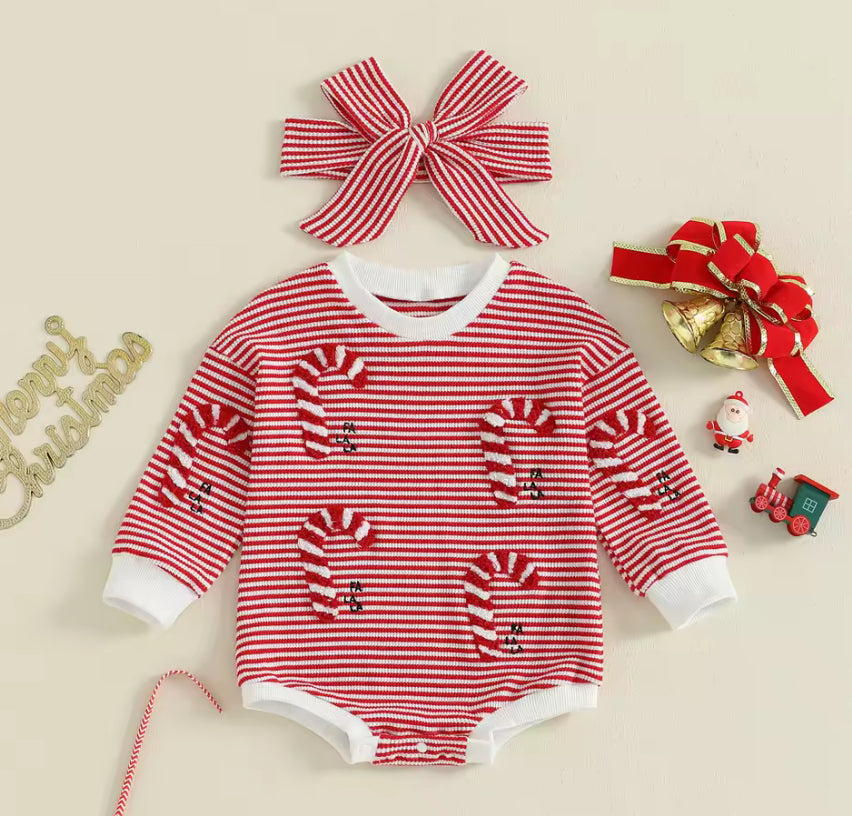 Red and white striped baby romper with candy cane design, accompanied by a matching headband and Christmas decorations on a beige background.