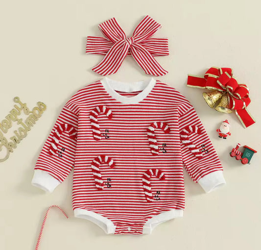Red and white striped baby romper with candy cane design, accompanied by a matching headband and Christmas decorations on a beige background.