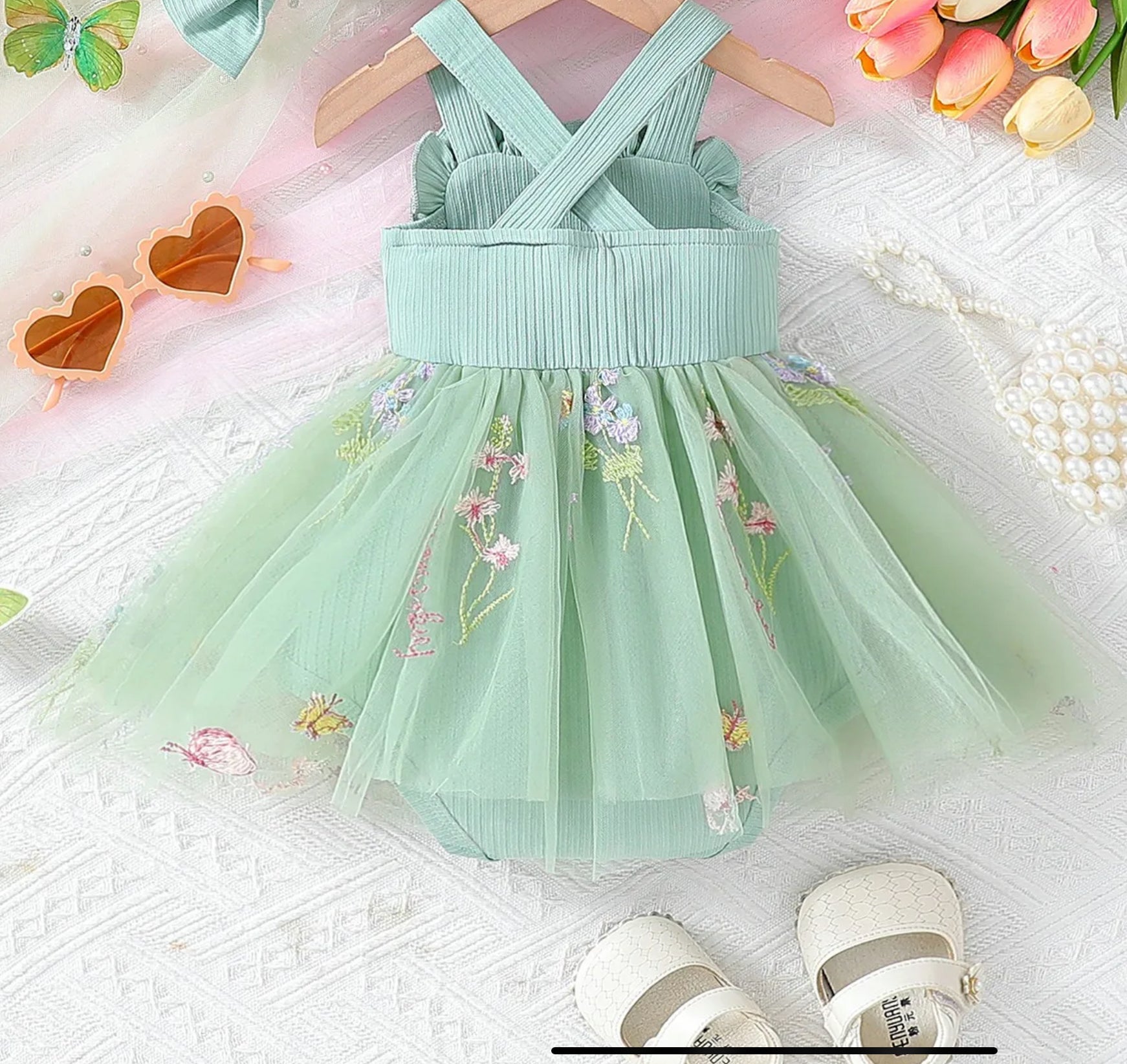 Mint green dress with floral embroidery on a textured surface with sunglasses and flowers in the background.