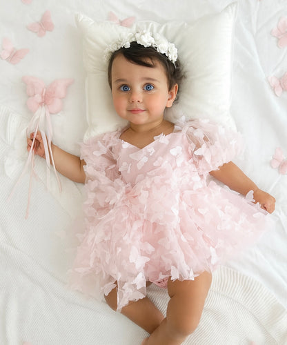Baby in a pink floral outfit lying on a white surface with pink flowers.