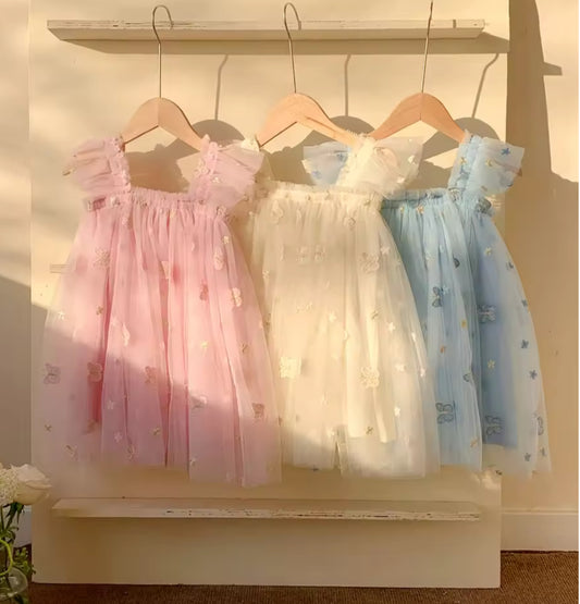 Three children's dresses in pink, white, and blue hanging on a rack.