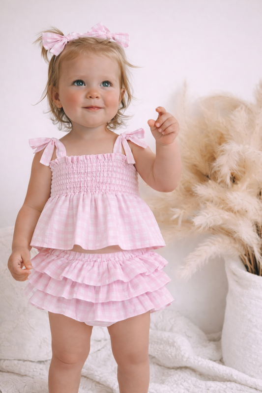 Baby girls clothing at baby boho - Young girl wearing a pink outfit with ruffles against a soft, neutral background