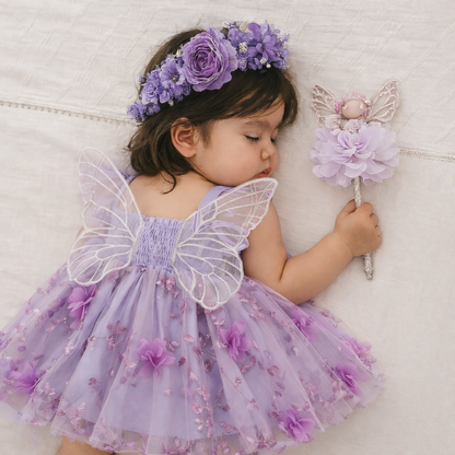 Baby boho- baby girls clothing -Child in a purple fairy costume with wings and a wand, lying on a textured surface.