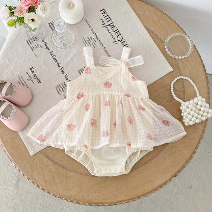 Baby dress with floral pattern on a wooden table with accessories
