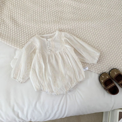 White baby dress on a white surface with brown shoes nearby
