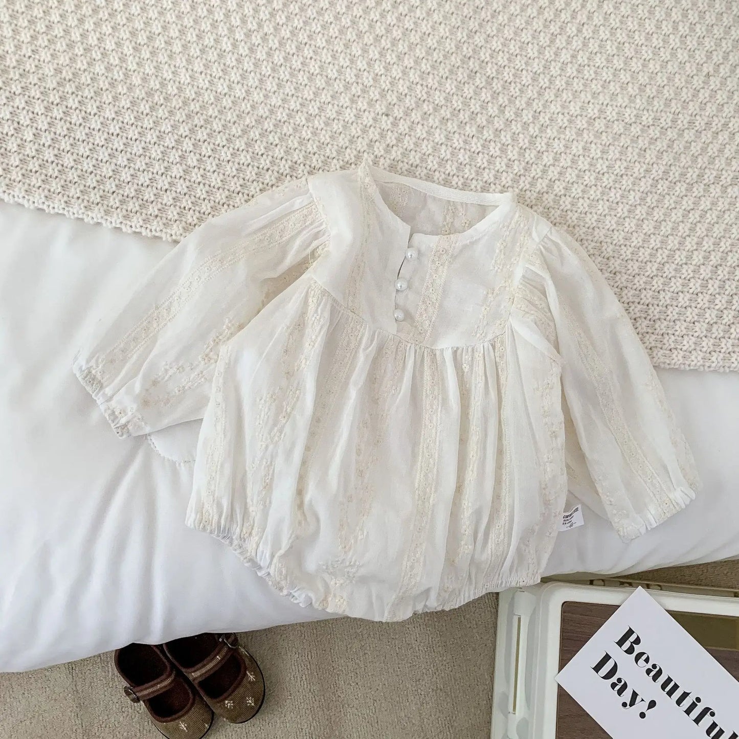 White baby dress on a textured surface with a pair of shoes and a book in the background.