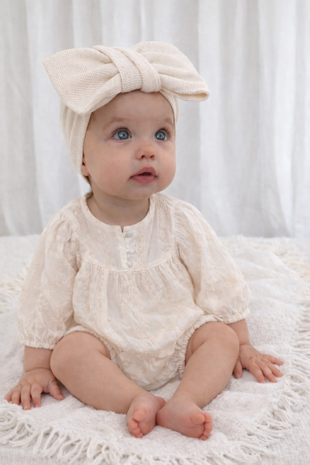 Cotton romoer by baby boho - baby girls clothing Baby wearing a cream-colored outfit and headband sitting on a white surface.