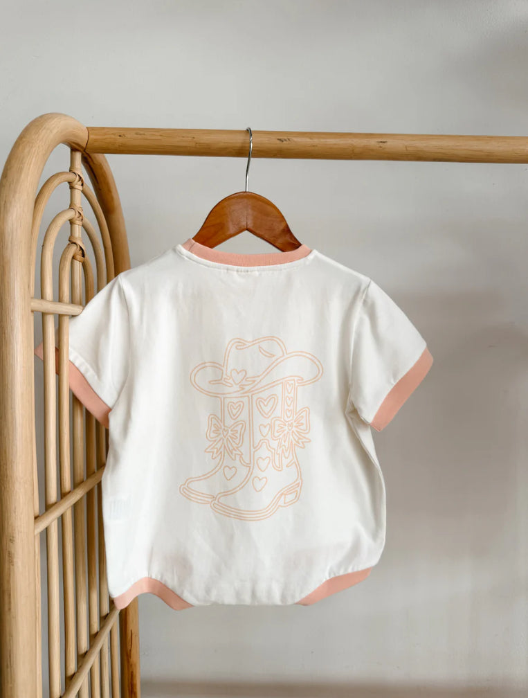 White baby romper with pink trim and embroidered design on a wooden hanger against a neutral background.