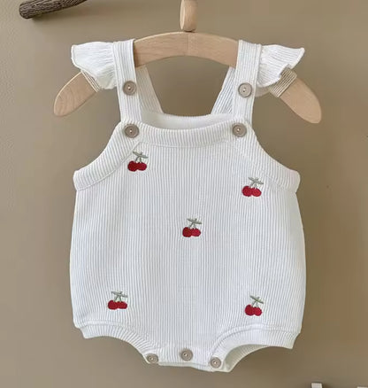 White baby romper with cherry designs on a wooden hanger against a beige background