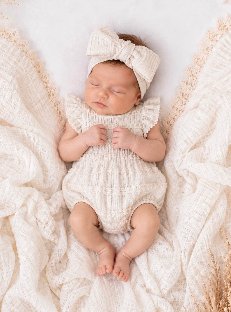 Newborn baby clothing - baby boho girll in a white outfit and headband lying on textured fabric