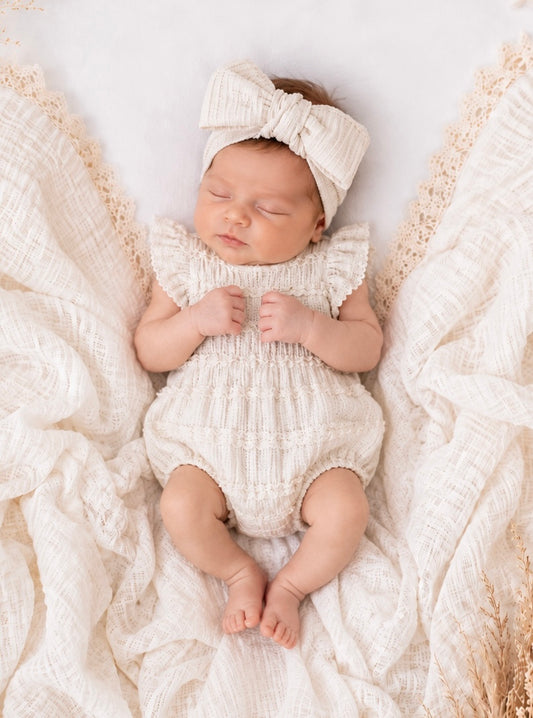 Newborn baby clothing - baby boho girll in a white outfit and headband lying on textured fabric