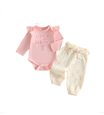 A two-piece baby outfit set featuring a light pink long-sleeve bodysuit with 'LITTLE sister' printed on the chest and ruffled shoulder details, paired with cream-colored textured pants with a pink bunny pattern and a matching bow tie waist.