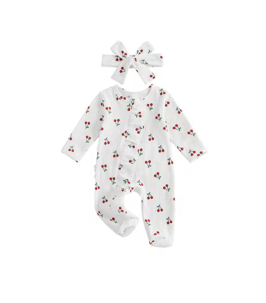 A baby footed romper in white ribbed fabric with a small red cherry print, shown with a matching white bow headband on a plain white background.